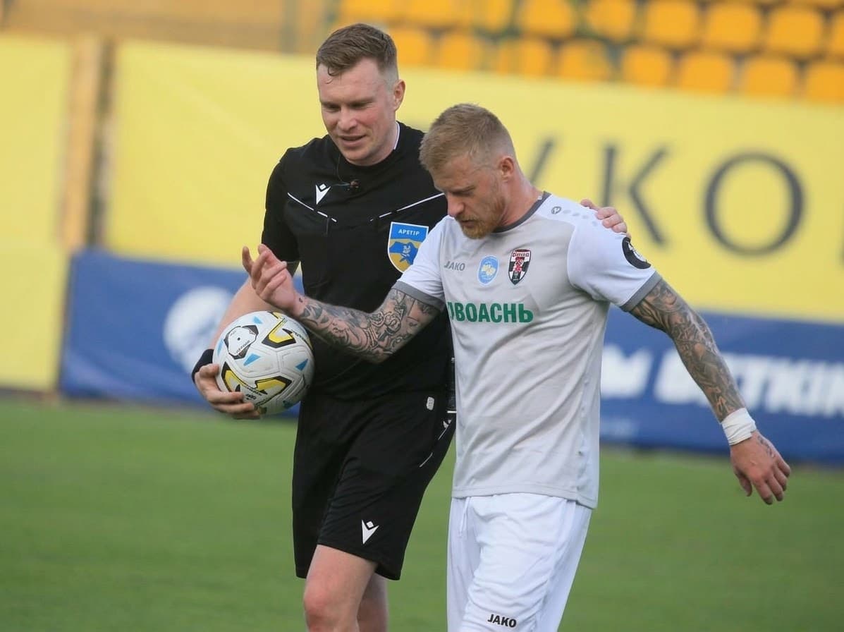 Referee Oleksandr Kalonov holding the match ball while walking off the pitch with a player after Bukovyna vs Obolon.