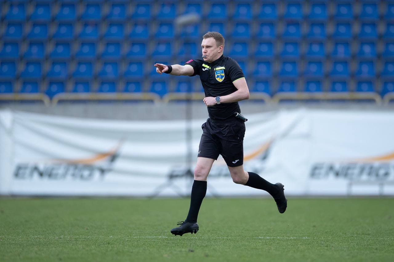Referee Oleksandr Kalonov running with whistle in mouth during Dnipro-1 vs Mynai at Dnipro Arena.